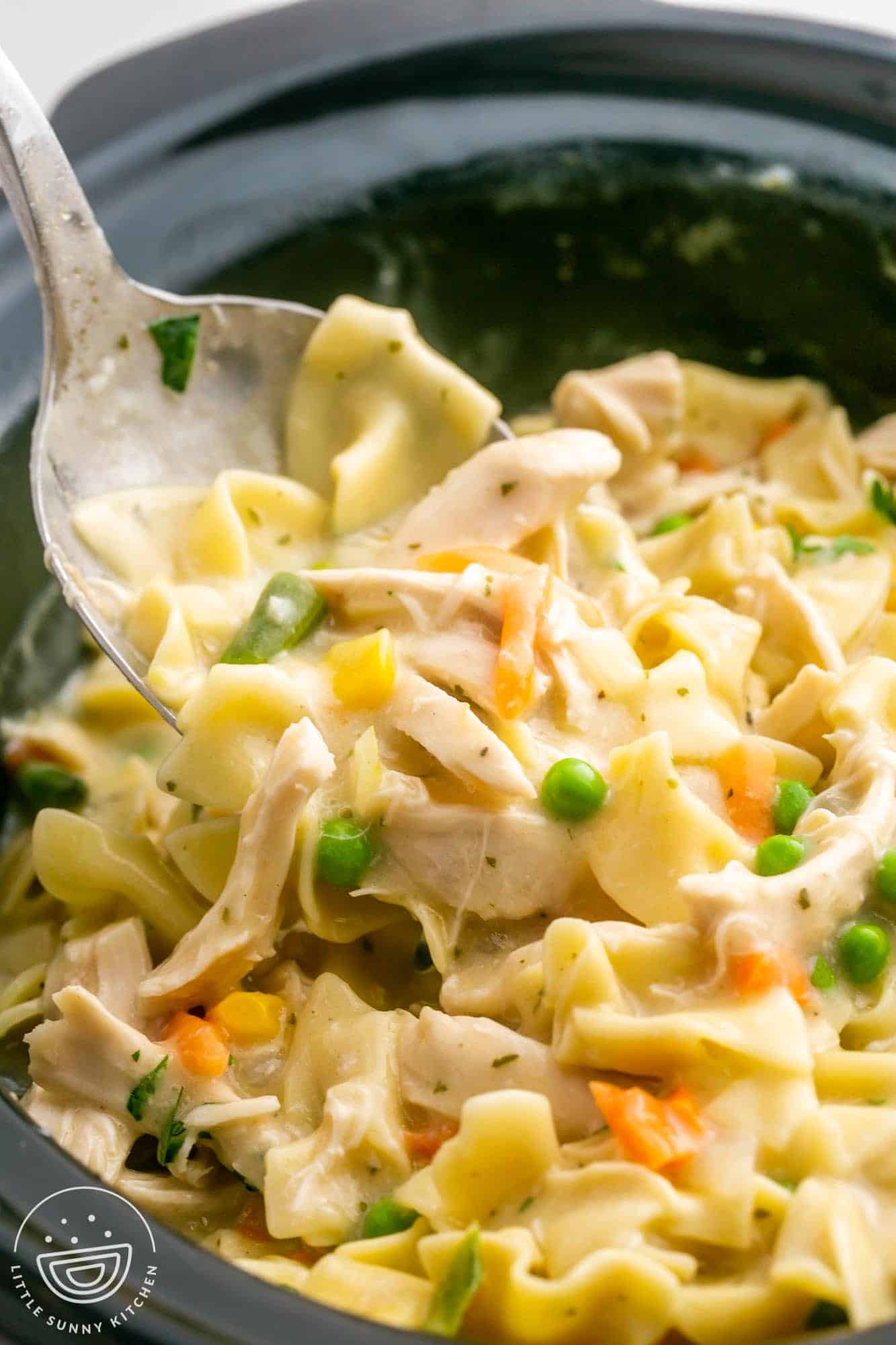 creamy chicken and noodles in a crockpot. A metal spoon is lifting some up to serve. 