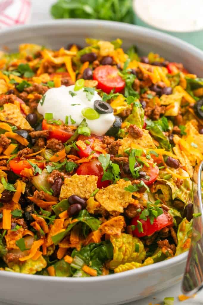 A large salad bowl with dorito taco salad and a dollop of sour cream