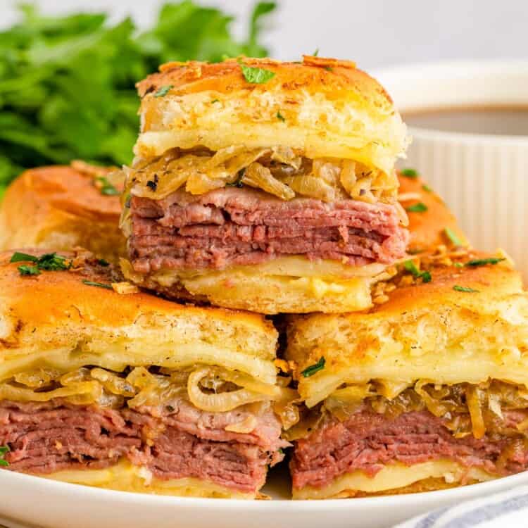 a plate filled with small french dip sandwiches. One sandwich is on top of the others.