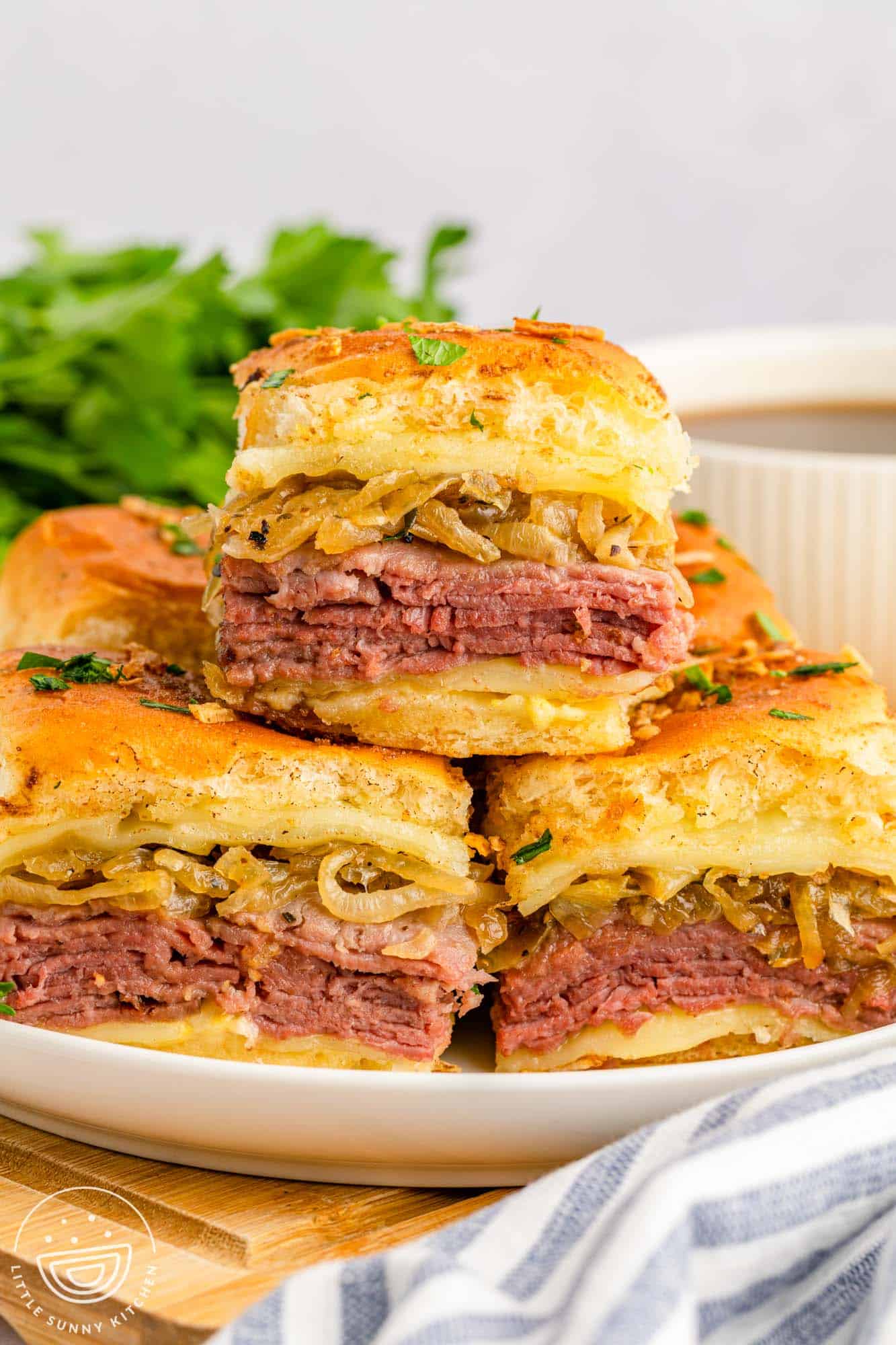 a plate filled with small french dip sandwiches. One sandwich is on top of the others.