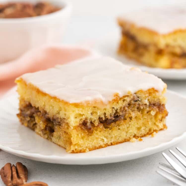 a square slice of honey bun cake with cinnamon sugar center, topped with glaze, on a plate.