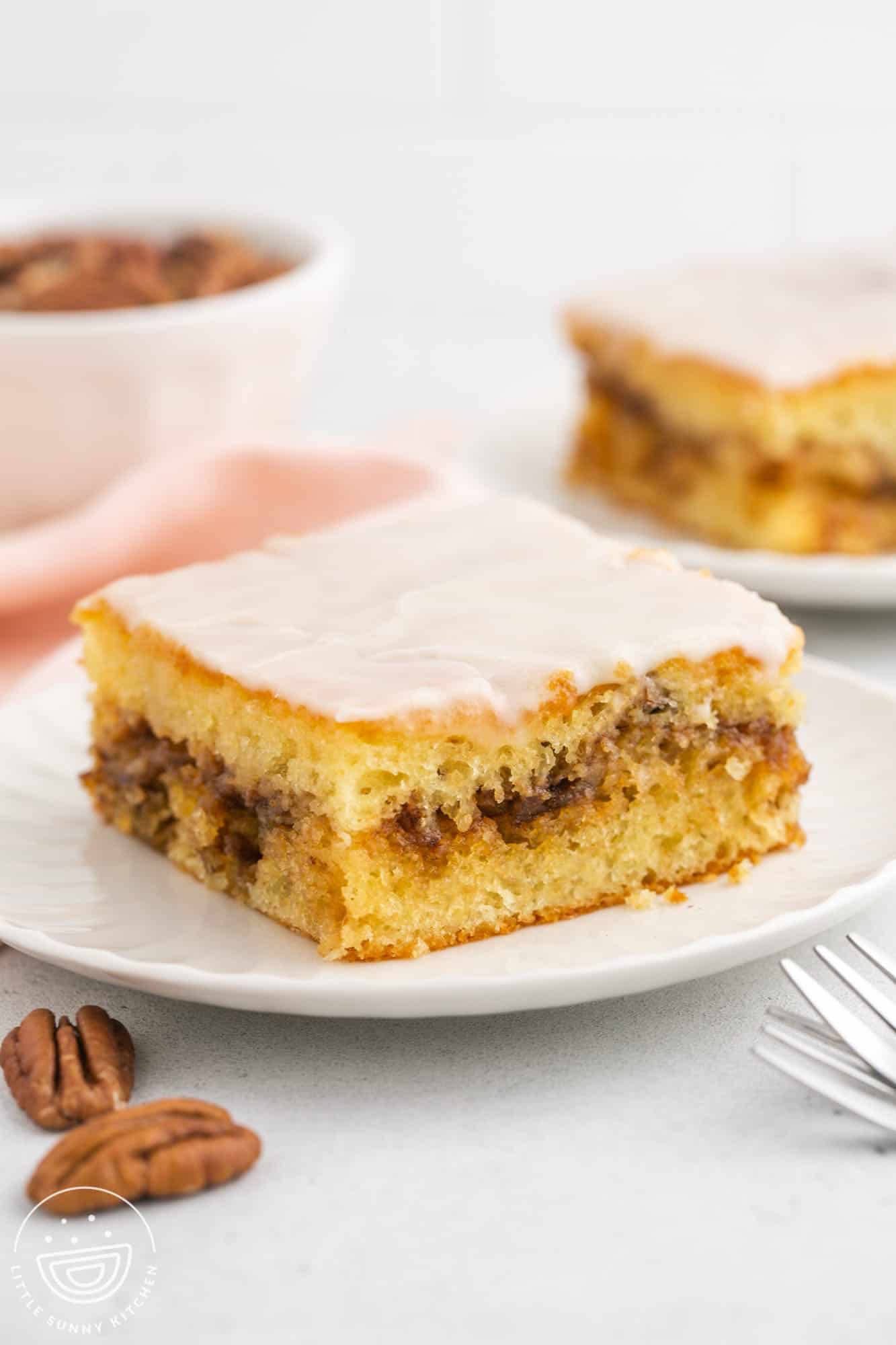 a square slice of honey bun cake with cinnamon sugar center, topped with glaze, on a plate. 