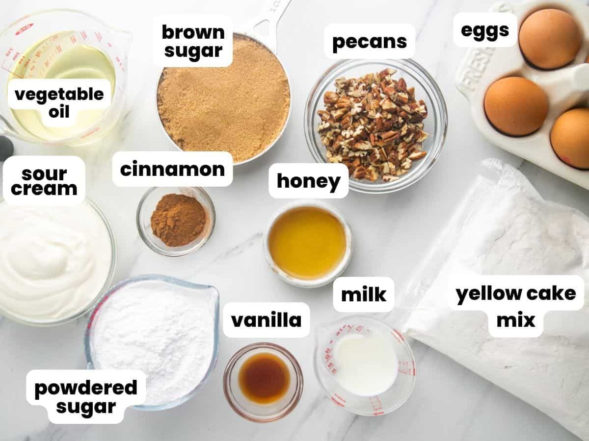 Ingredients for making a honey bun cake, measured into separate small bowls and arranged on a counter. Each ingredient is labeled with a text box overlay.