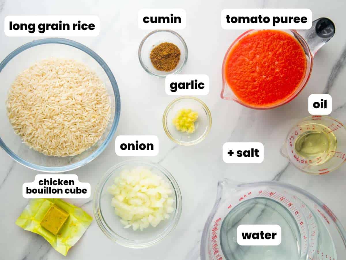 The ingredients needed to make mexican rice from scratch, including rice, tomatoes, water, and spices, all in separate clear bowls, on a counter, viewed from above.