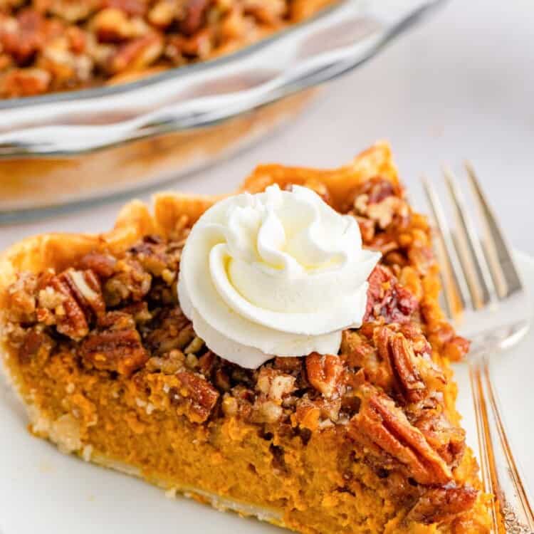 a large wedge of pumpkin pie topped with pecans on a plate. There's a dollop of whipped cream on top and a fork next to the slice.