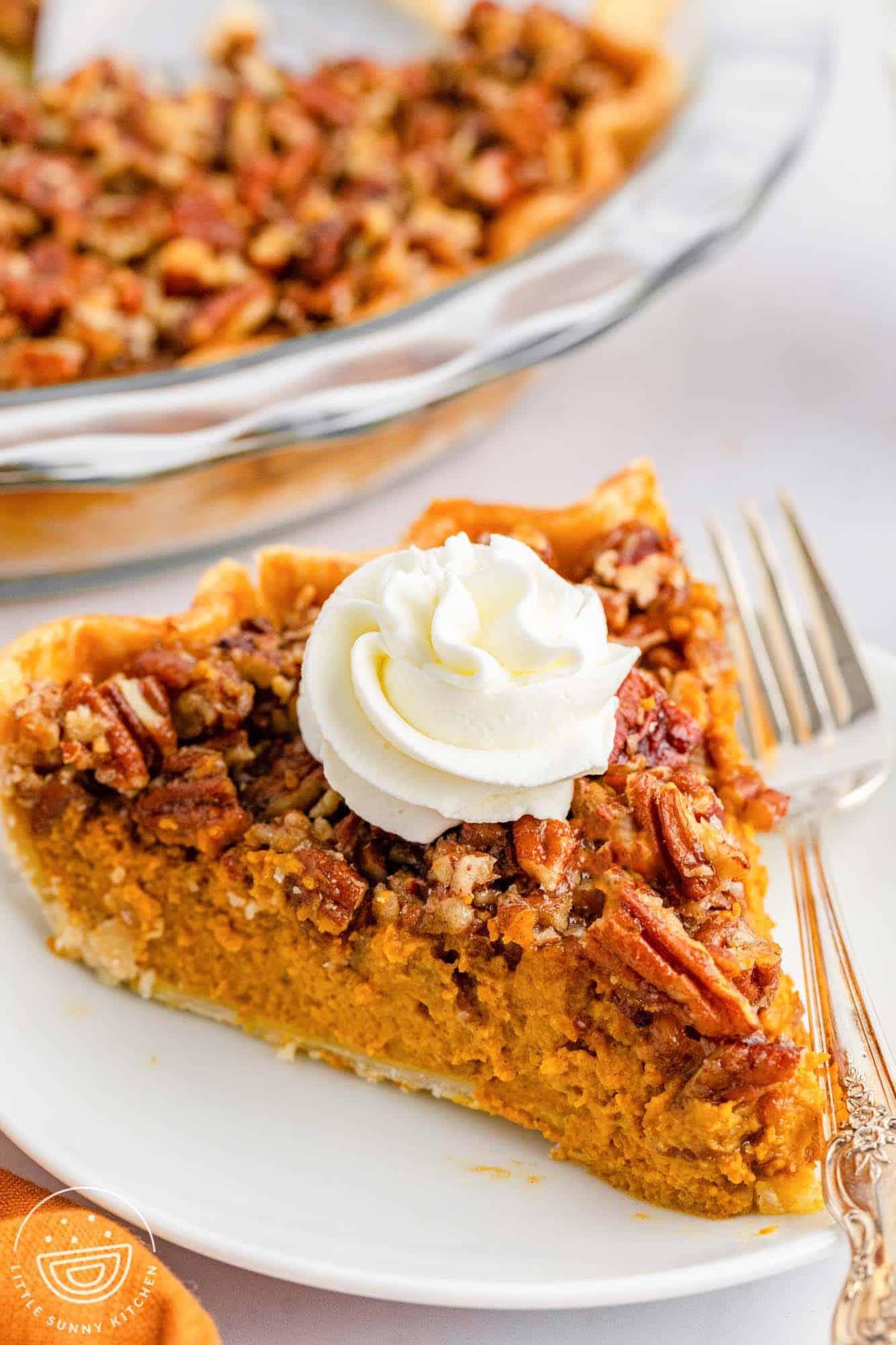 a large wedge of pumpkin pie topped with pecans on a plate. There's a dollop of whipped cream on top and a fork next to the slice. 
