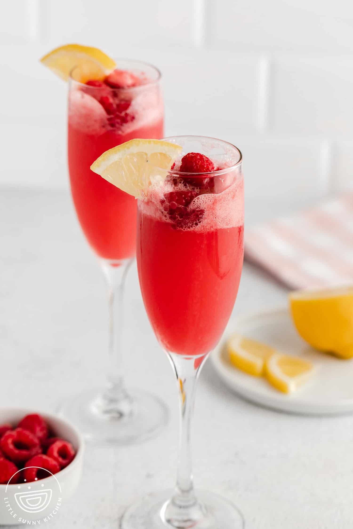 2 flute glasses with raspberry bellini, fresh raspberries and lemon slices