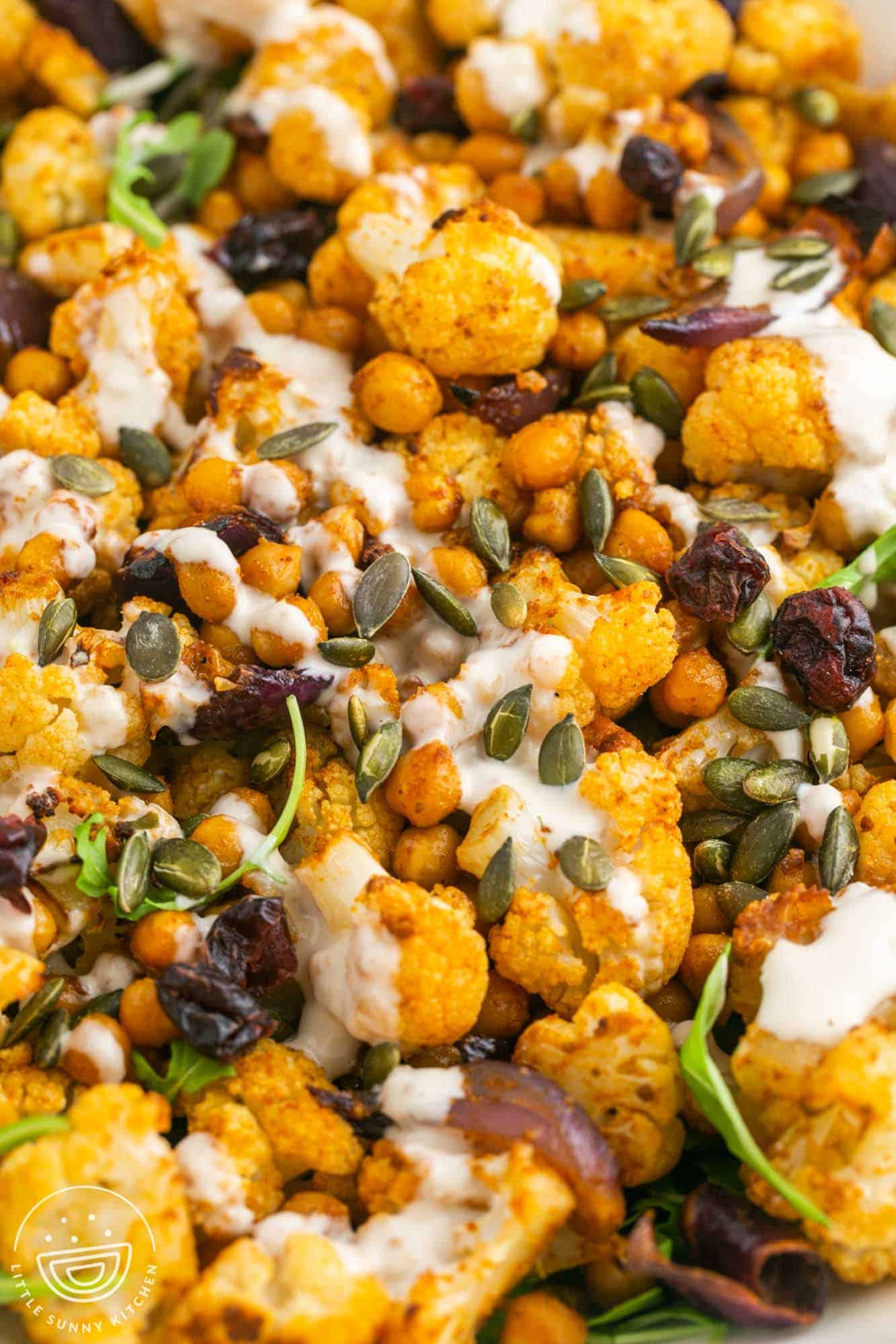 Close up shot of cauliflower salad with chickpeas, tahini dressing, pepitas, and cranberries.