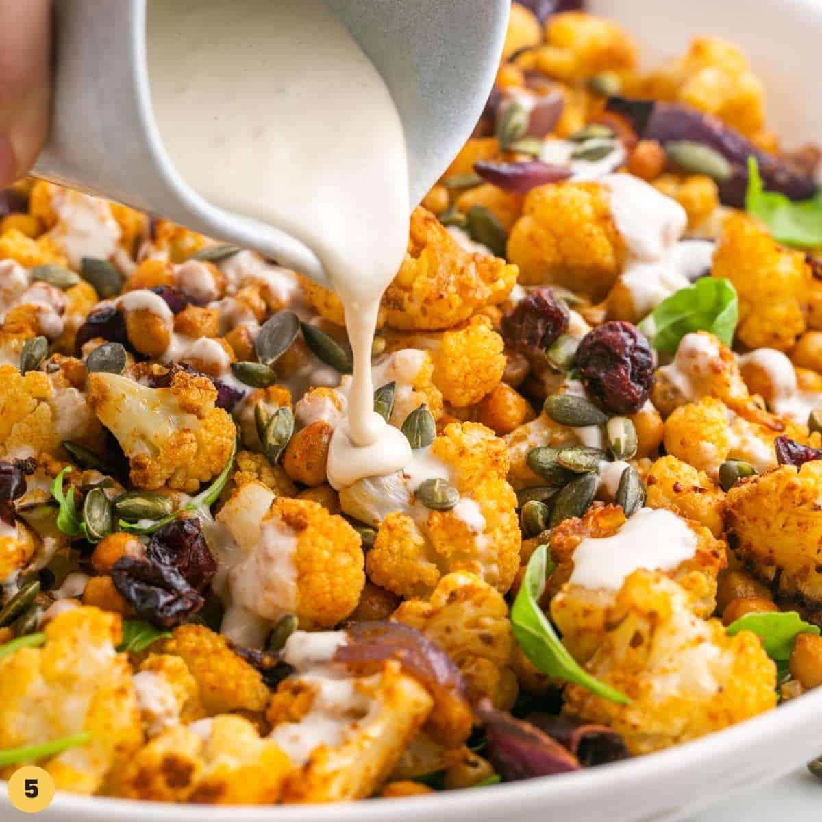 Tahini dressing being drizzle over roasted cauliflower salad