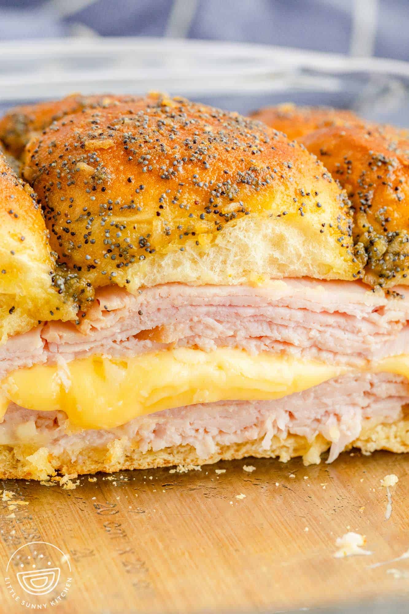 A side view of a pan of turkey and cheese sliders on hawaiian rolls. The havarti cheese is melty in between layers of thinly sliced turkey
