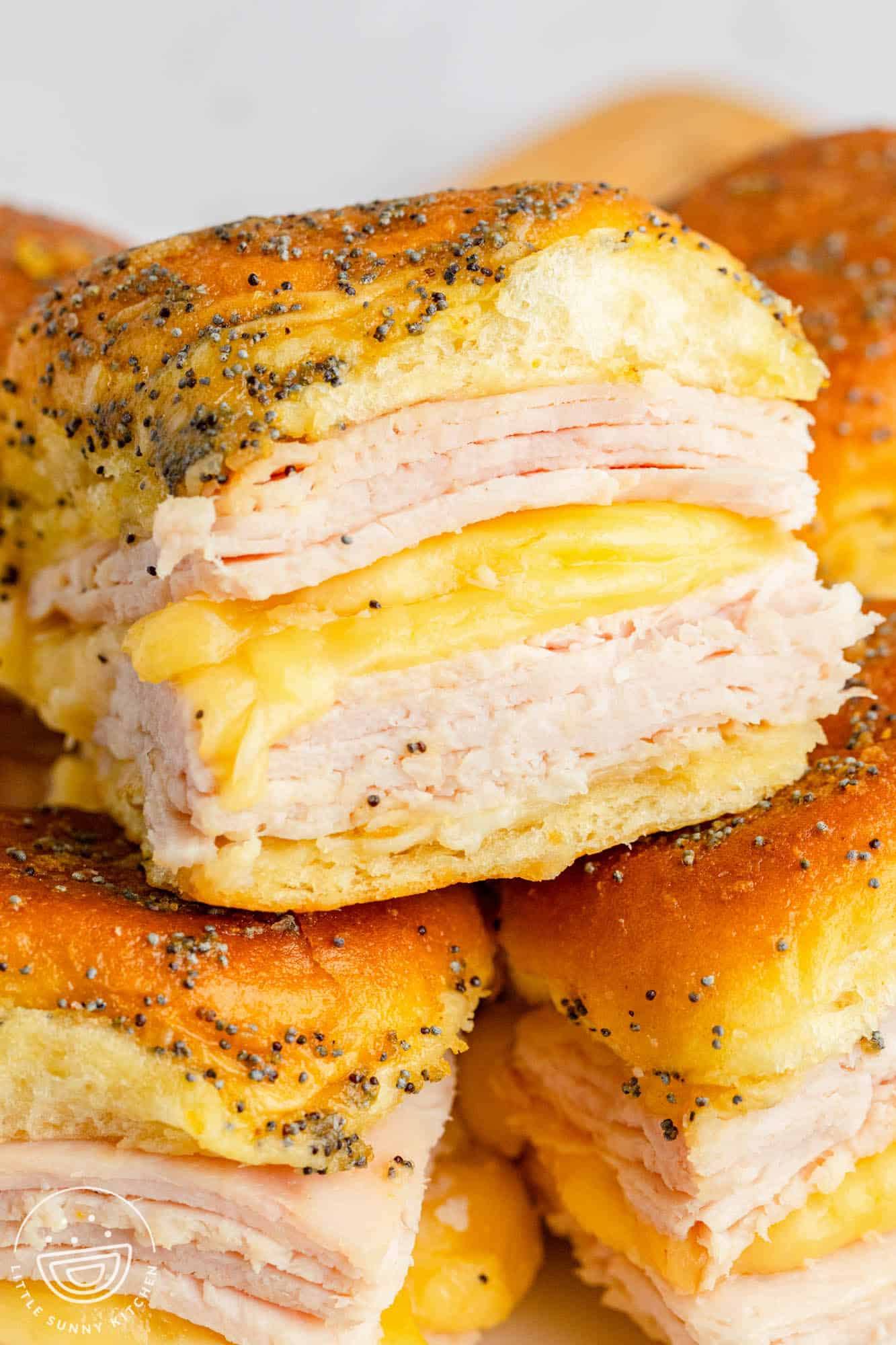 Turkey and cheese sliders stacked on top of each other. There are two layers of turkey with melty cheese in between.