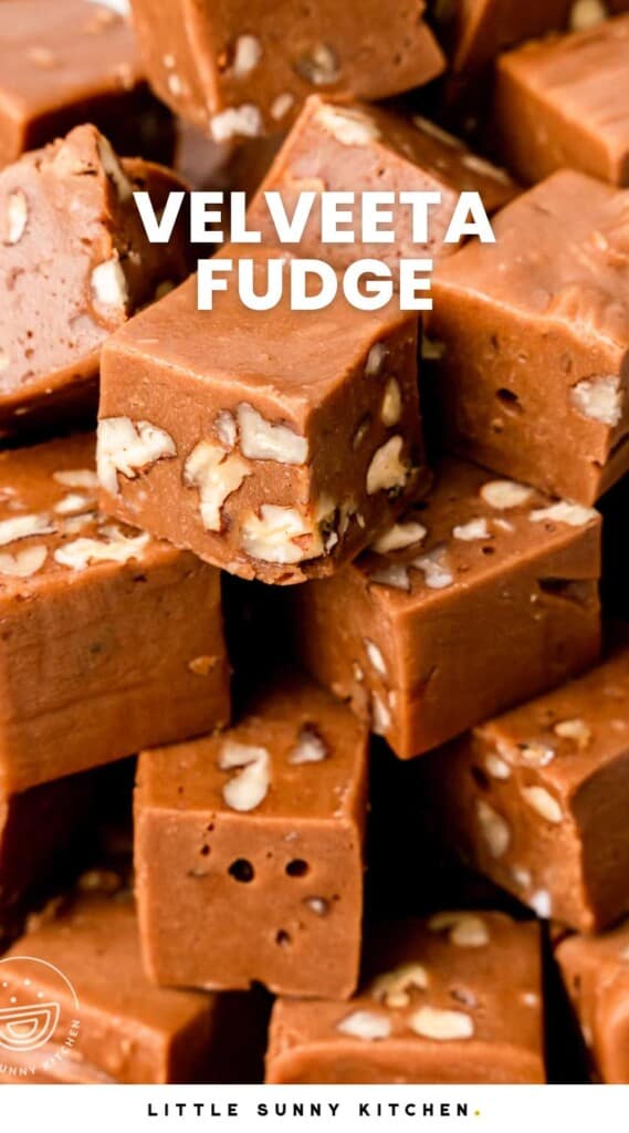 A stack of square pieces of cheese fudge with walnuts inside. Text overlay says "velveeta fudge" in capital letters.