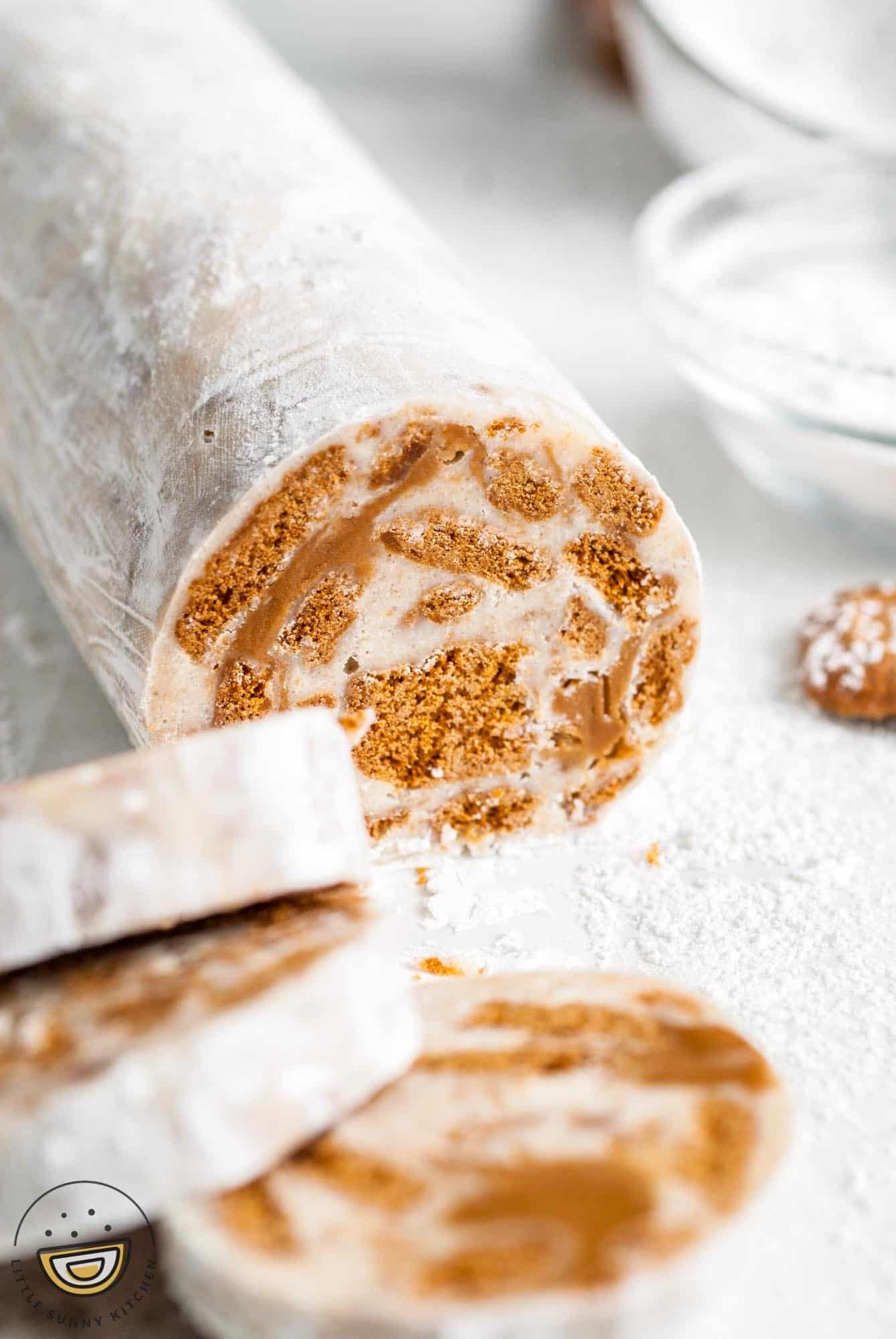 white chocolate biscoff salami dusted in powdered sugar. Three slices have been removed from the front.