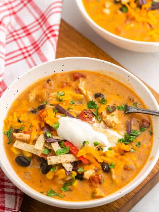 A white bowl with chicken enchilada soup, and a spoon. Placed on a wooden board.