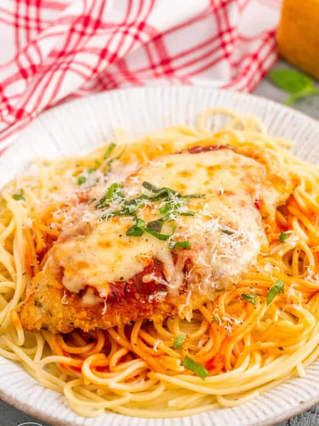 A chicken parmesan cutlet on top of spaghetti, on a white plate.