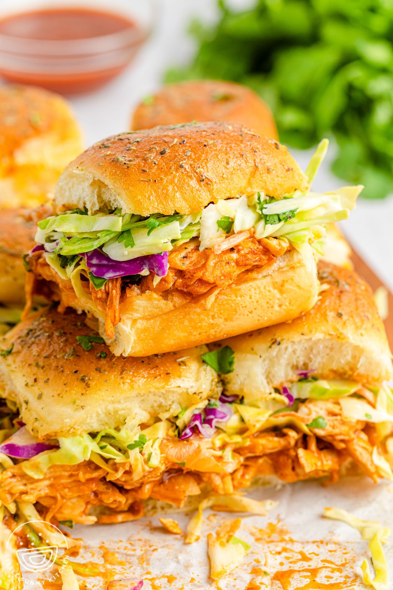 a stack of bbq chicken sliders on hawaiian rolls with coleslaw. 