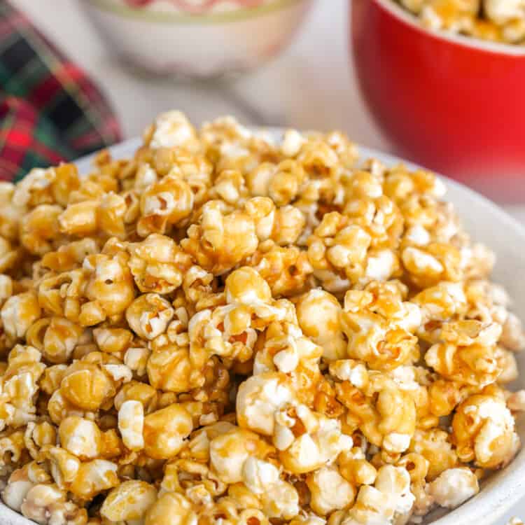 a large bowl of caramel popcorn with smaller bowls behind it.