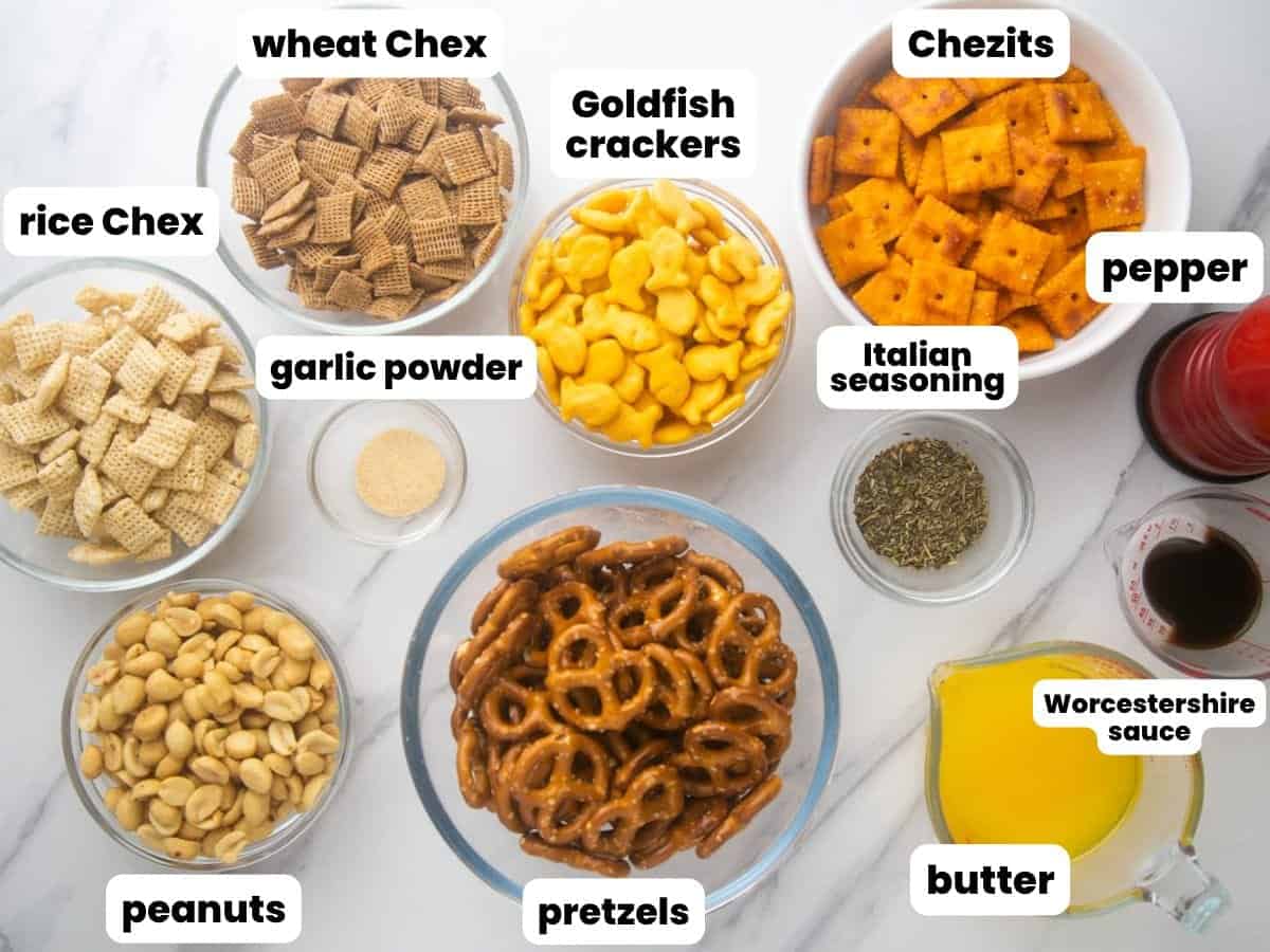 The ingredients needed to make homemade chex mix, all in separate bowls, arranged on a counter. Text boxes label each ingredient.