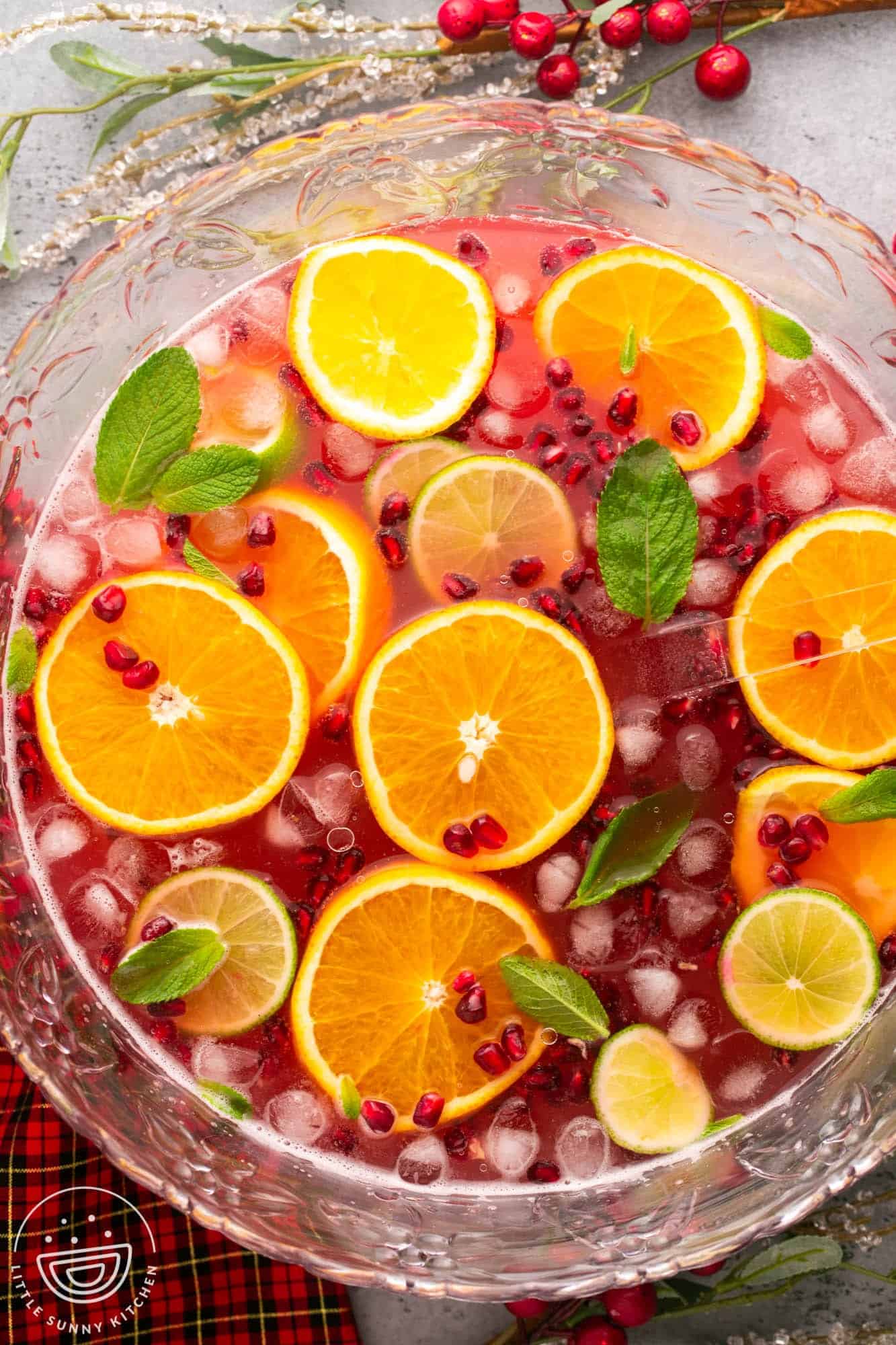 Overhead shot of a punch bowl filled with cranberry punch, sliced orange, lime slices, ice, mint leaves and pomegranate seeds.