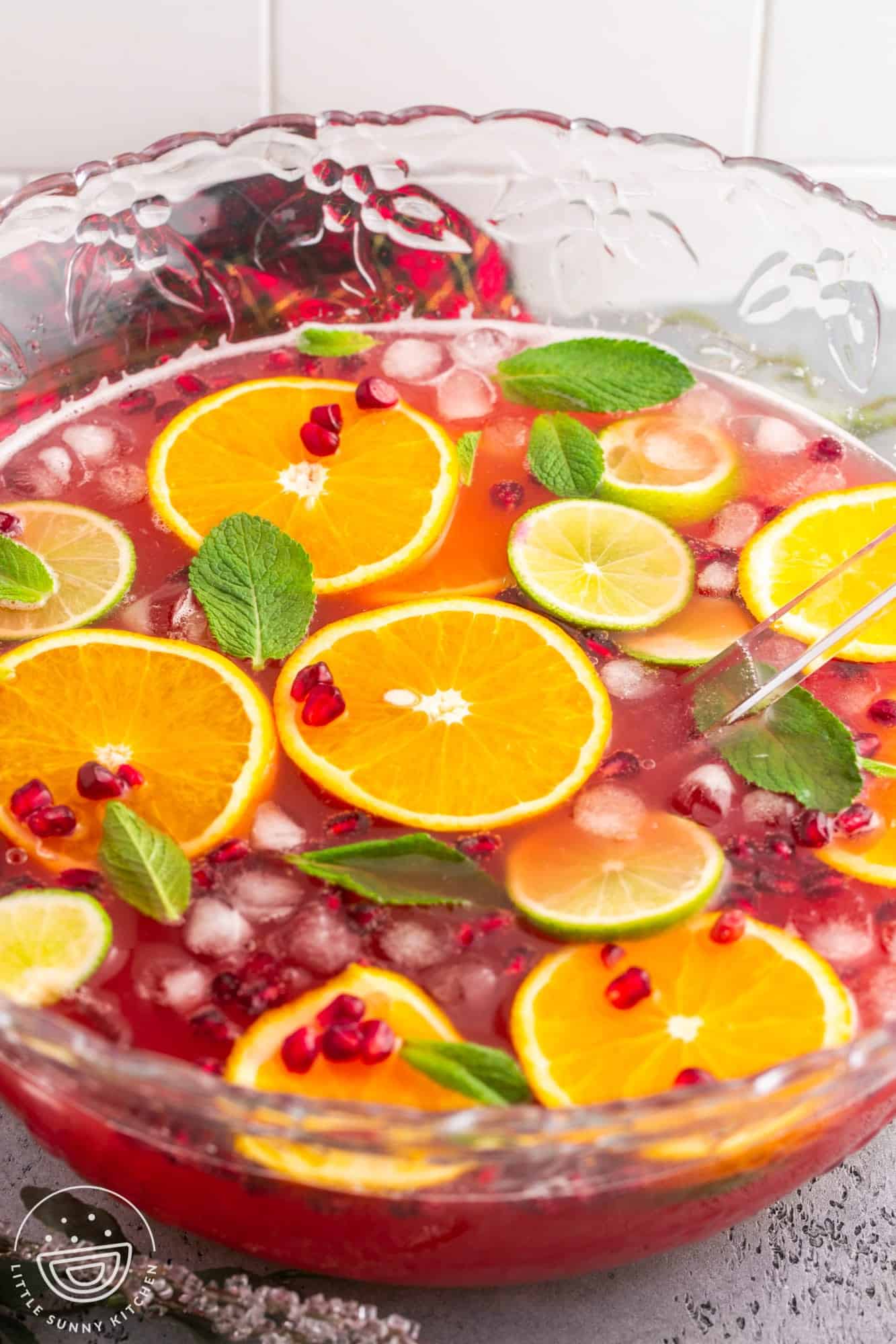 A bowl of cranberry punch with orange slices, pomegranate seeds, ice, and mint leaves.