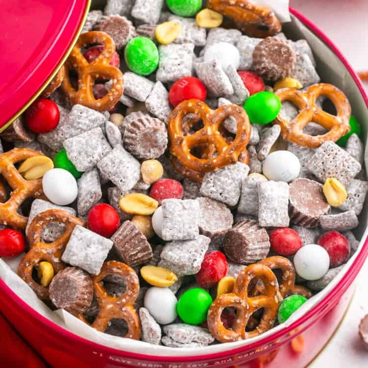 a red bowl filled with christmas puppy chow with pretzels and holiday m&ms.