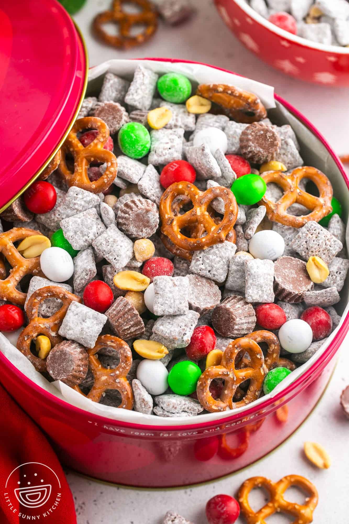 a red bowl filled with christmas puppy chow with pretzels and holiday m&ms.