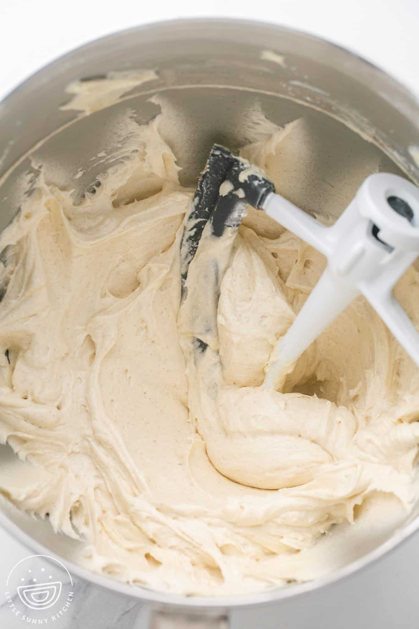 Whipped cinnamon cream cheese frosting in a large bowl with a paddle attachment