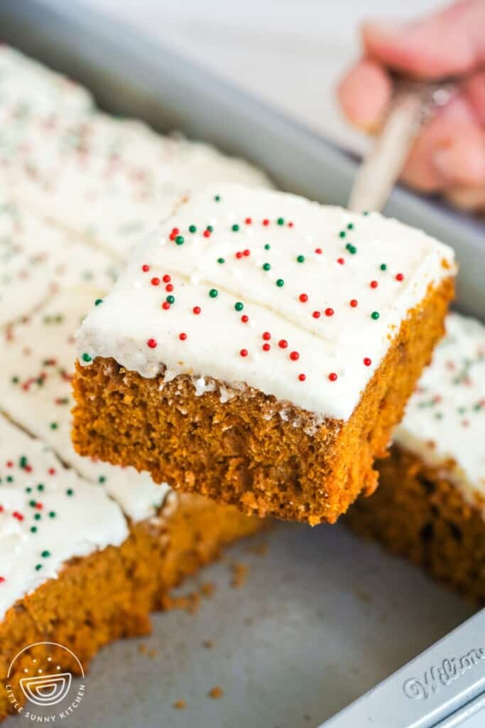 a spatula holding up a square of frosted gingerbread cake over the pan.