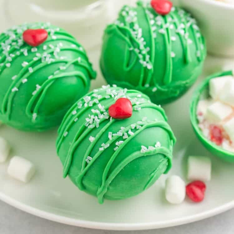 Three green hot chocolate bombs with heart sprinkles on them for grinch theme