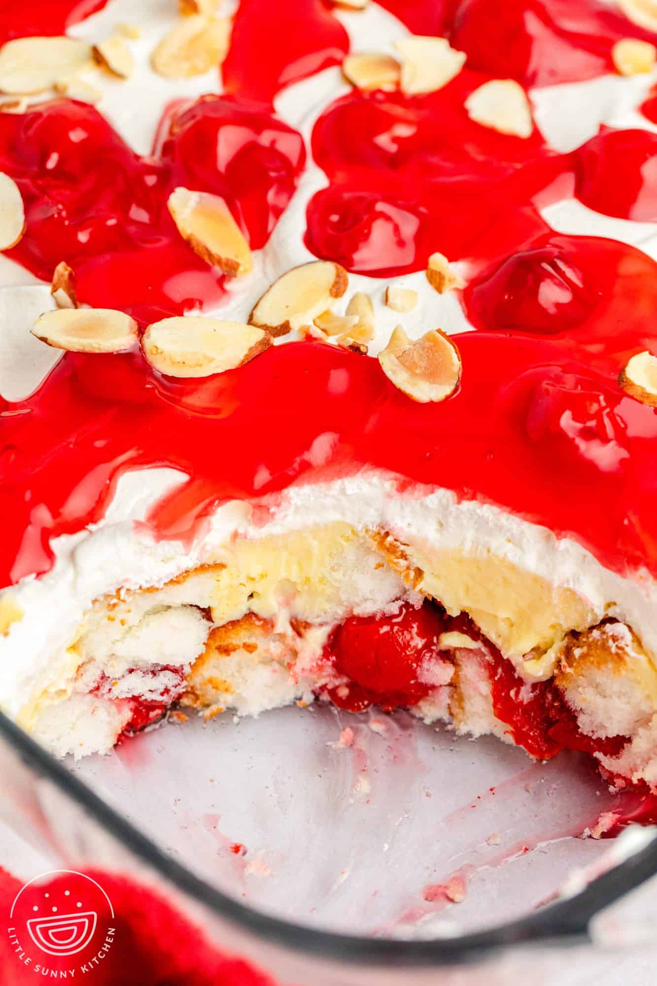 heaven on earth cake topped with cherry pie filling and slivered almonds, in a glass pan. A serving has been removed from the front corner to show the texture inside.
