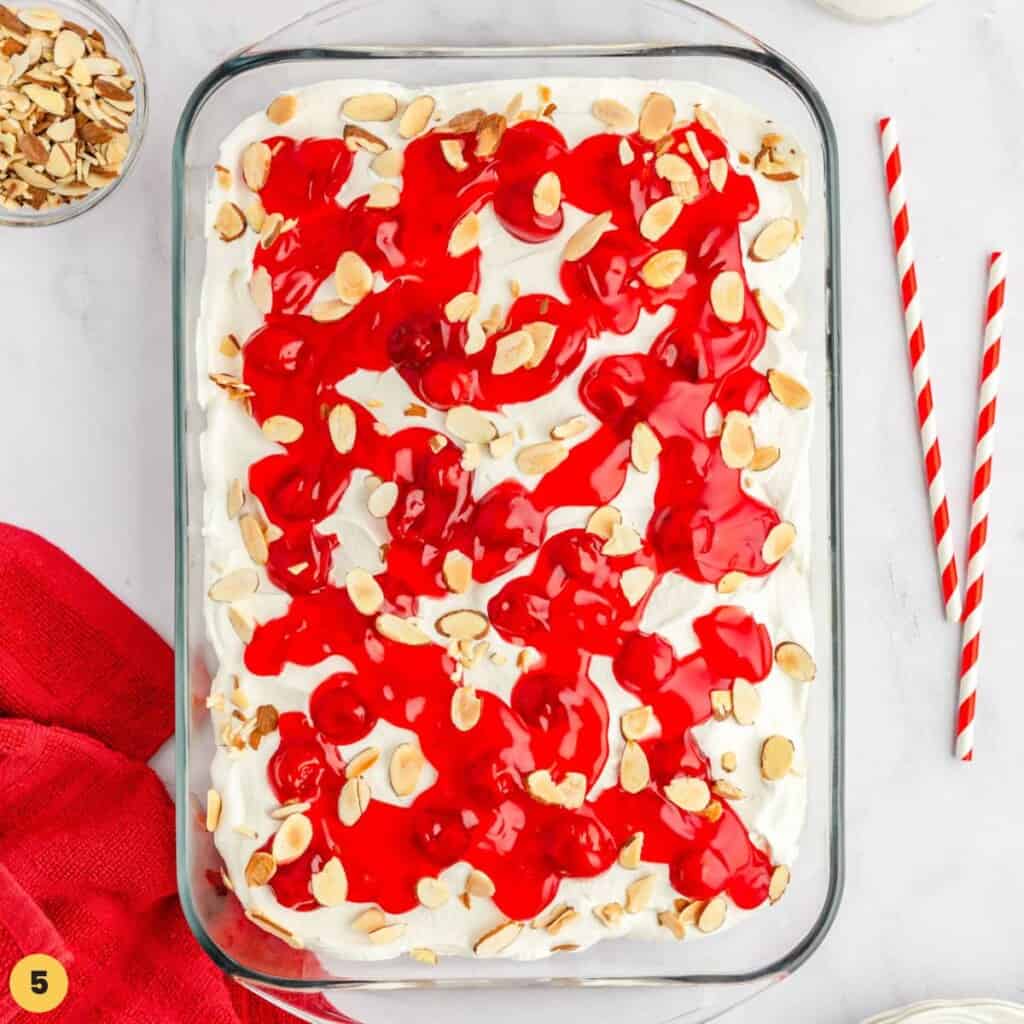 heaven on earth cake in a glass pyrex pan, topped with cool whip, cherries, and almonds.