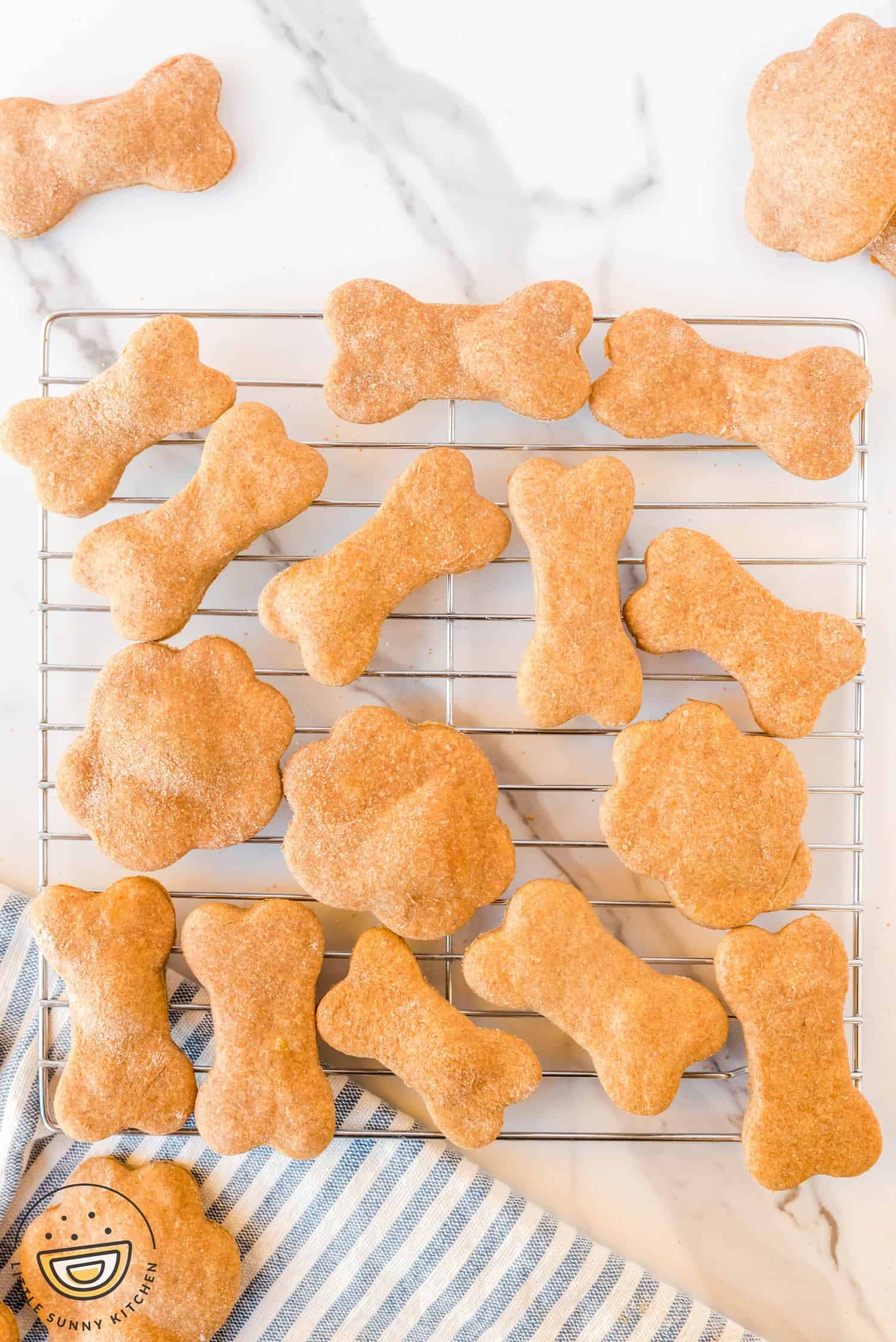 Homemade dog treats cut into bone and paw shapes, cooling on a rack.