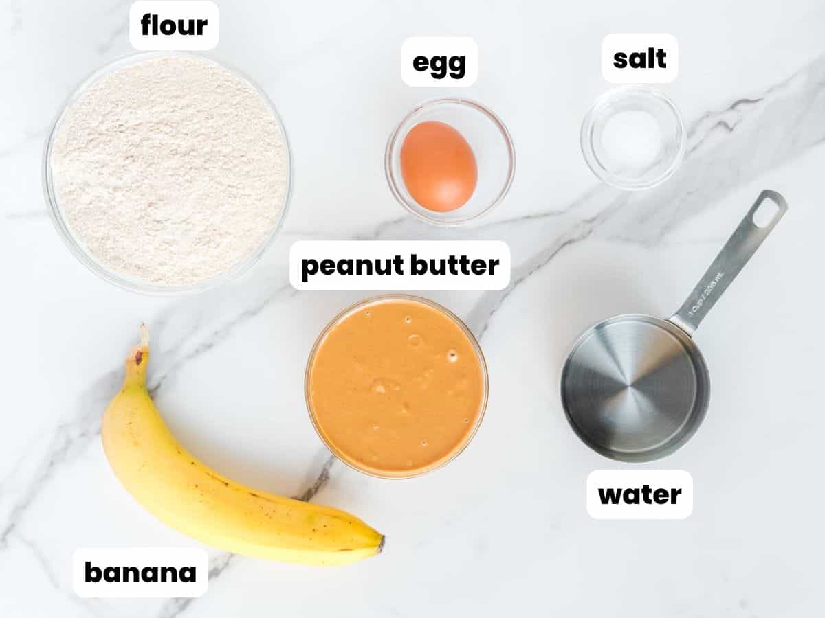 the ingredients for making peanut butter banana dog treats, measured into bowls, arranged on a counter. Each is labeled with a text box overlay