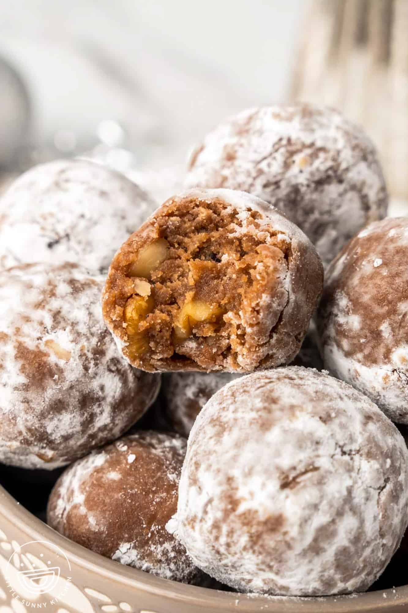 a pile of powdered sugar rum balls. One on top has been bitten into to show the interior texture. 