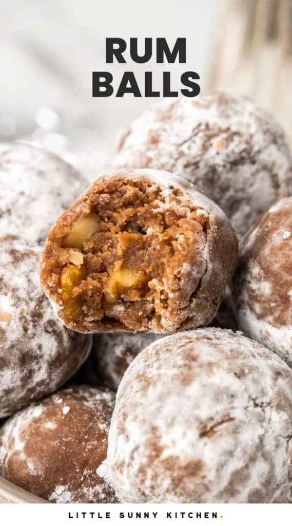 a pile of powdered sugar rum balls. One on top has been bitten into to show the interior texture. Text overlay at top of photo says "rum balls"