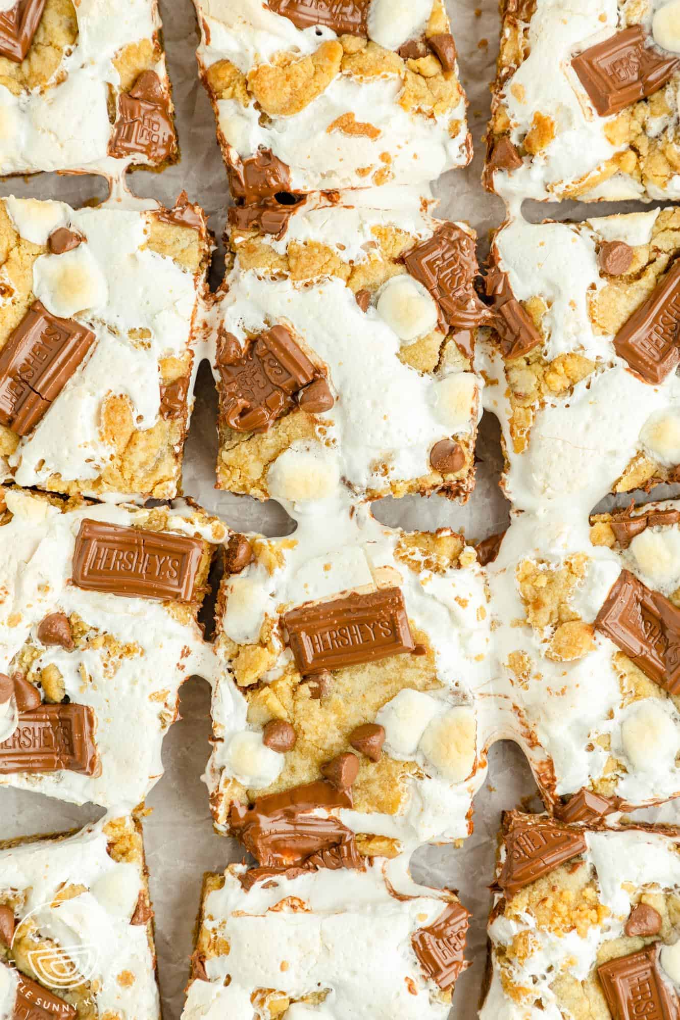 overhead photo of a batch of smores bars with marshmallows and chocolate bars on top. The bars have been cut apart to show the gooey marshmallow creme.