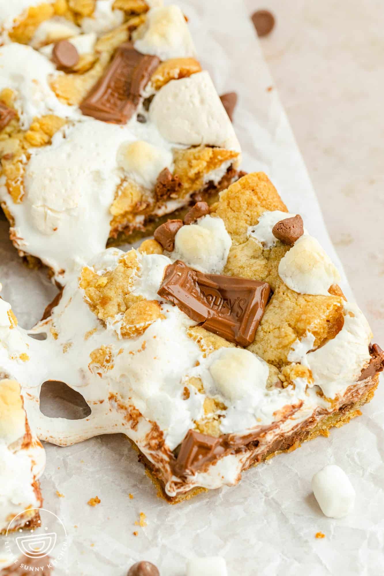 s'mores cookie bars cut on a piece of parchment paper. The marshmallow cream is gooey.