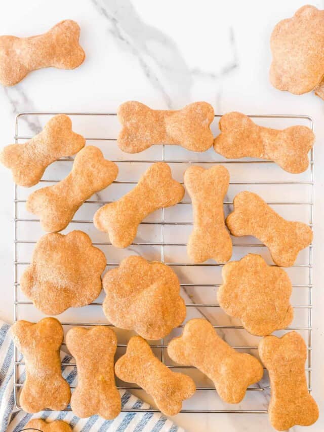 Homemade dog treats cut into bone and paw shapes, cooling on a rack.
