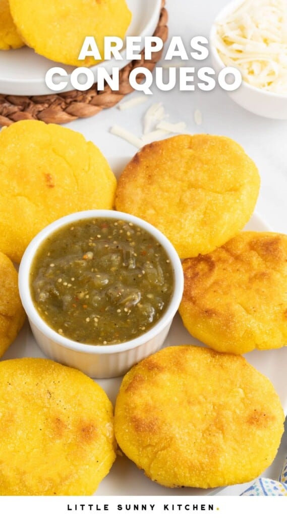 arepas con queso with tomatillo salsa in a small bowl in the center of a platter. Text overlay says "arepas con queso"
