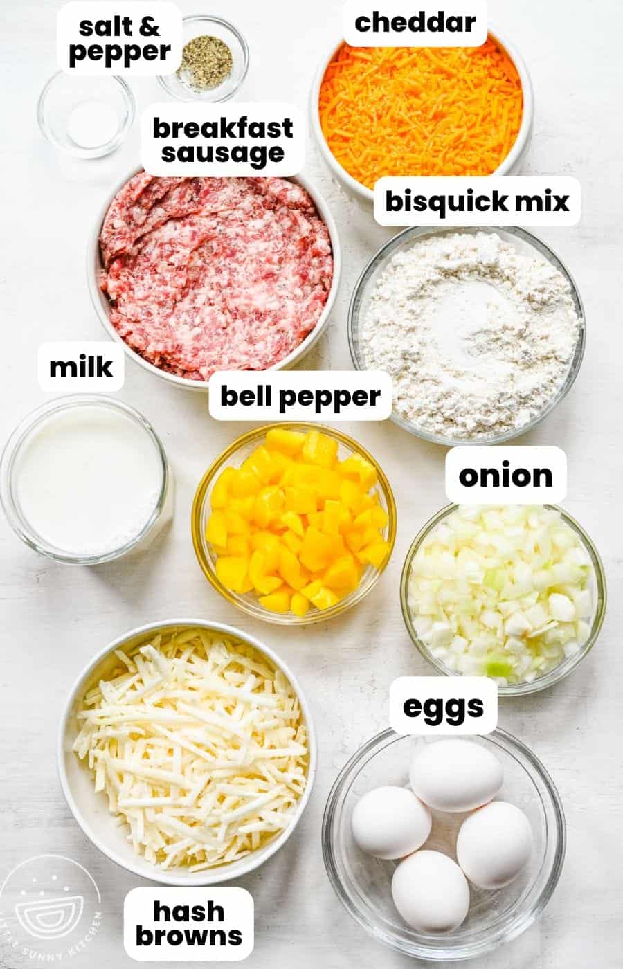 The ingredients needed to make biscuit breakfast casserole, all in small bowls, arranged on a counter. Included are eggs, sausage, peppers and onions, and cheese.
