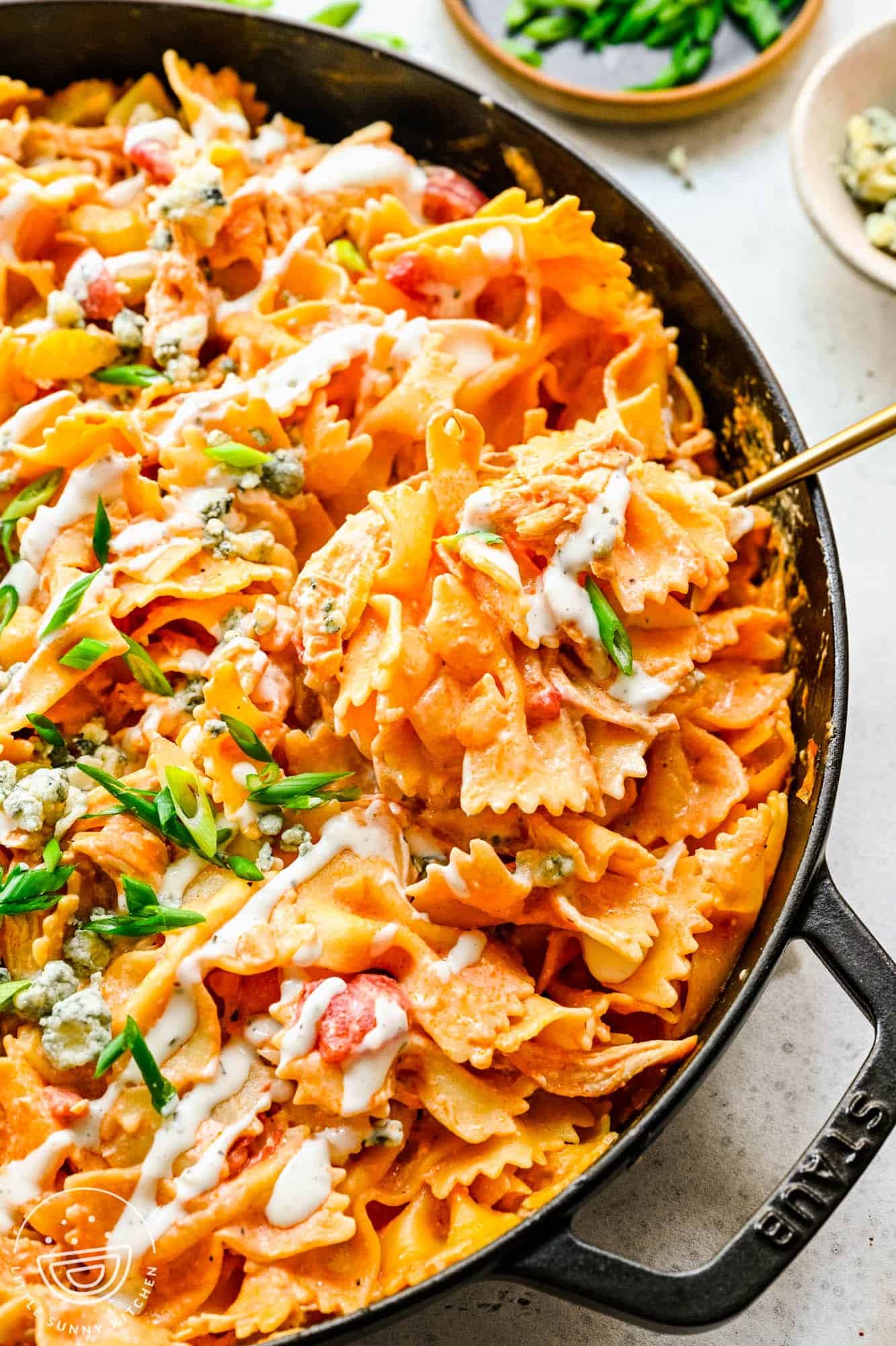 creamy buffalo chicken bowtie pasta being served from a cast iron skillet.