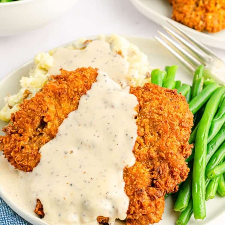 Chicken fried steak served over mashed potatoes with green beans on the side, and white peppery gravy on top.