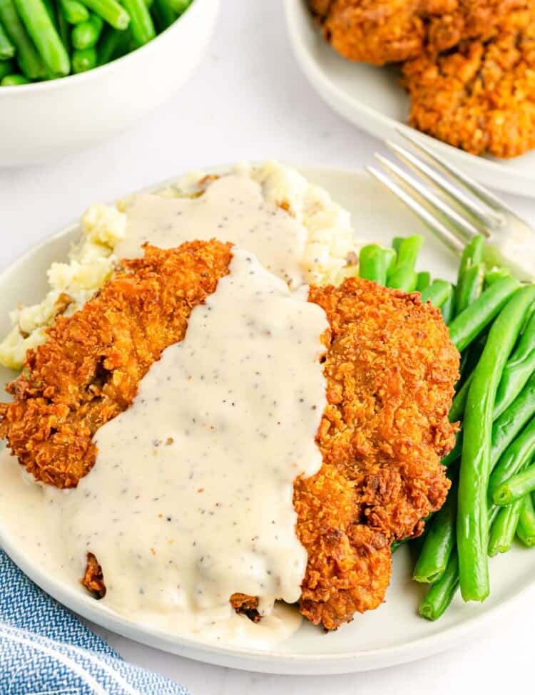 Chicken fried steak served over mashed potatoes with green beans on the side, and white peppery gravy on top.