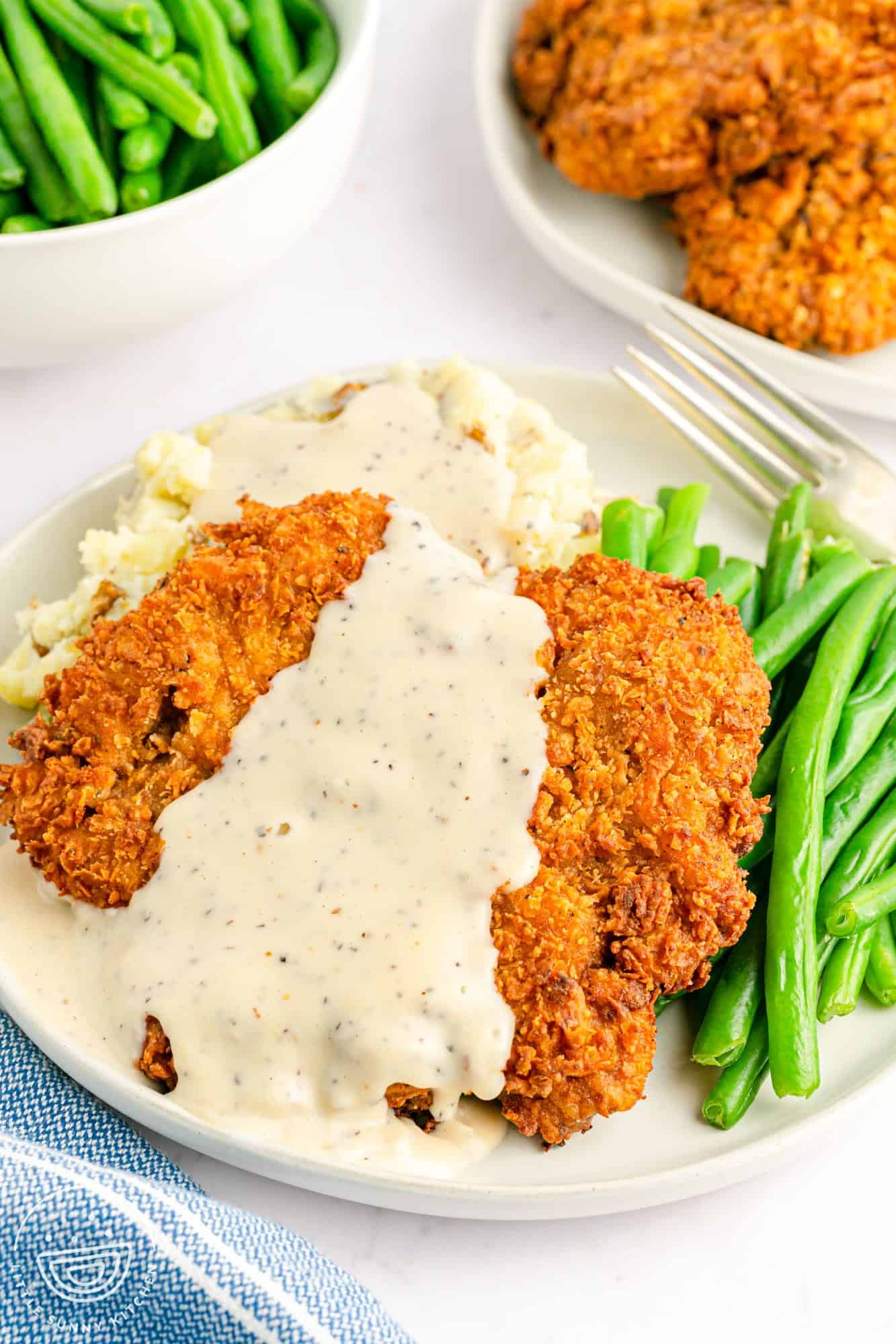 Chicken fried steak served over mashed potatoes with green beans on the side, and white peppery gravy on top.