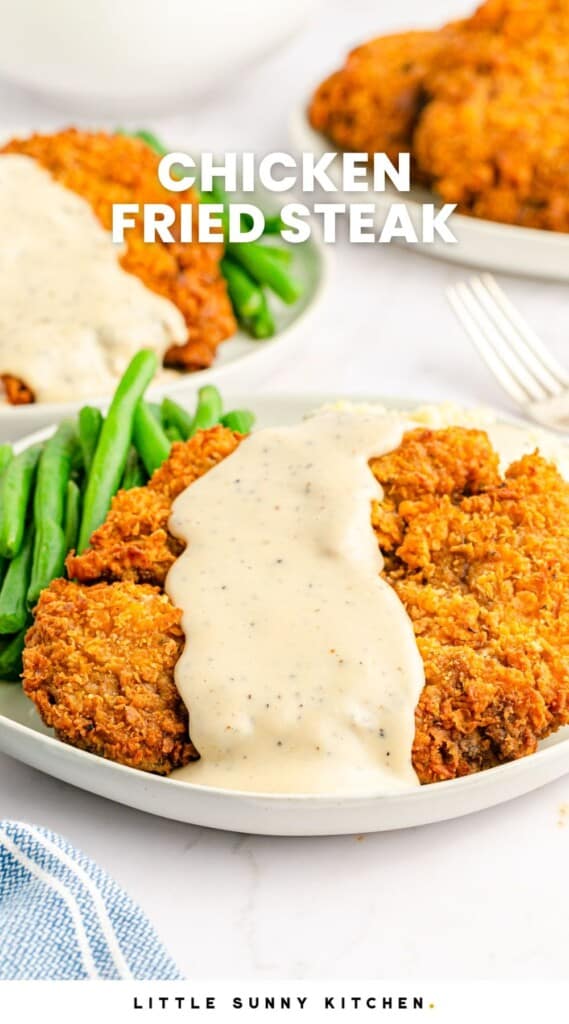 Chicken fried steak served over mashed potatoes with green beans on the side, and white peppery gravy on top. And overlay text that says "chicken fried steak"