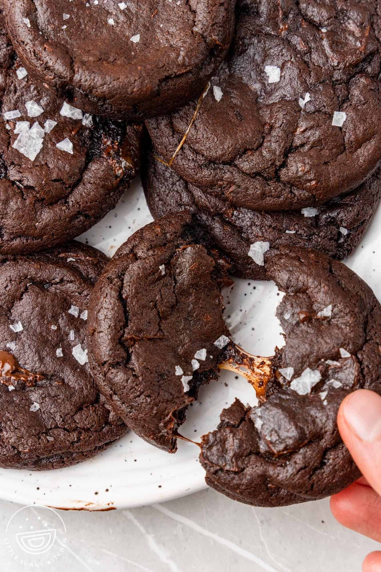 a hand pulling apart a chocolate cookie to reveal melted caramel in the center.