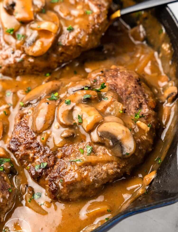 2 hamburger steaks in gravy with mushrooms, in a cast iron skillet.