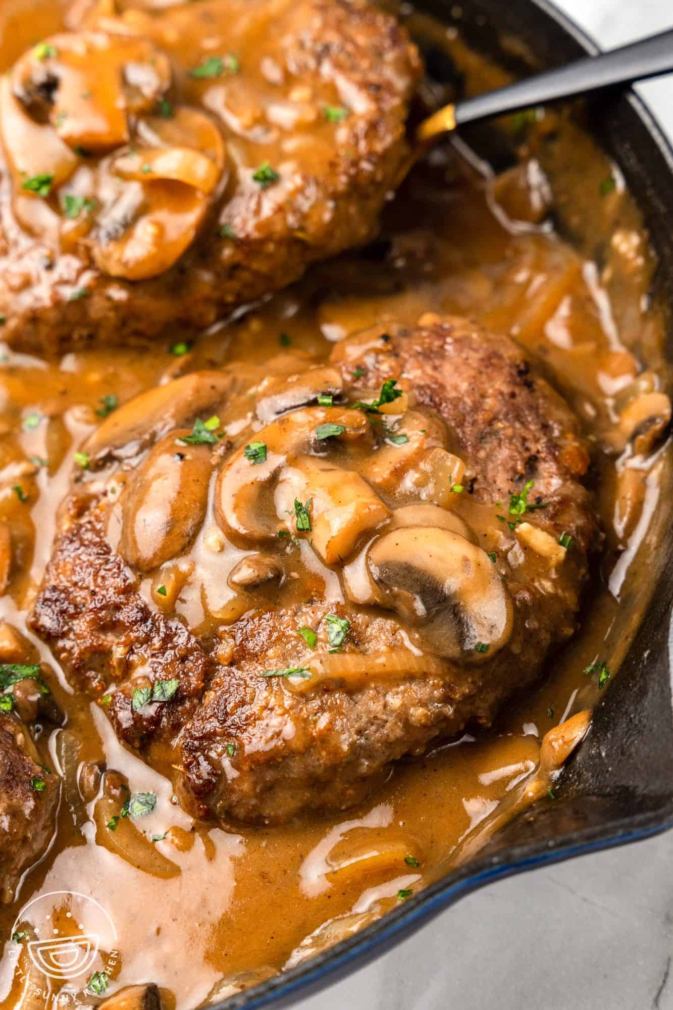 2 hamburger steaks in gravy with mushrooms, in a cast iron skillet.