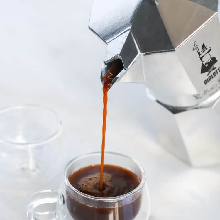 Pouring a cup of coffee from a Bialetti moka pot into a small espresso coffee cup