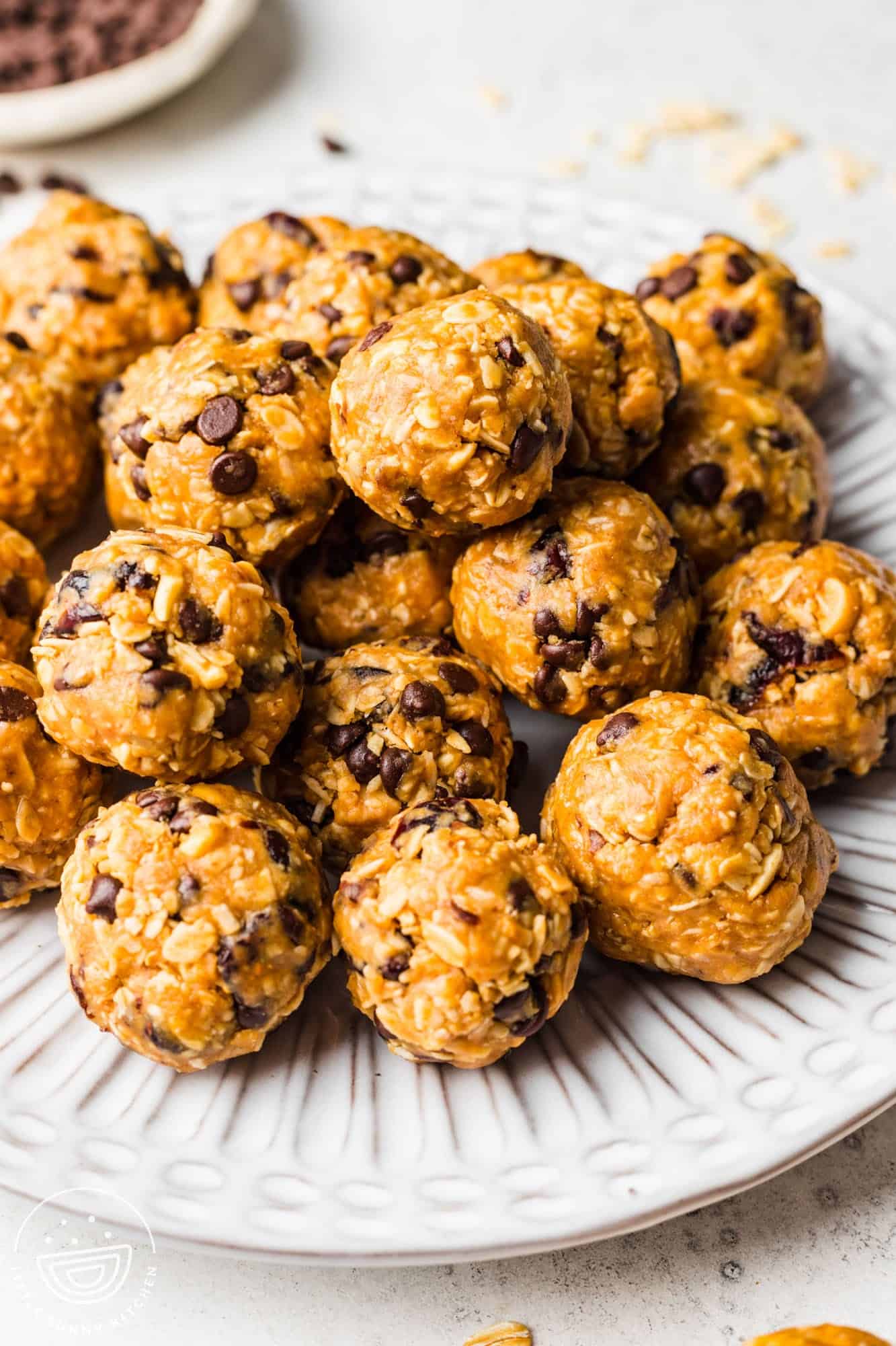 a ridged white plate stacked with chocolate chip oatmeal balls. 